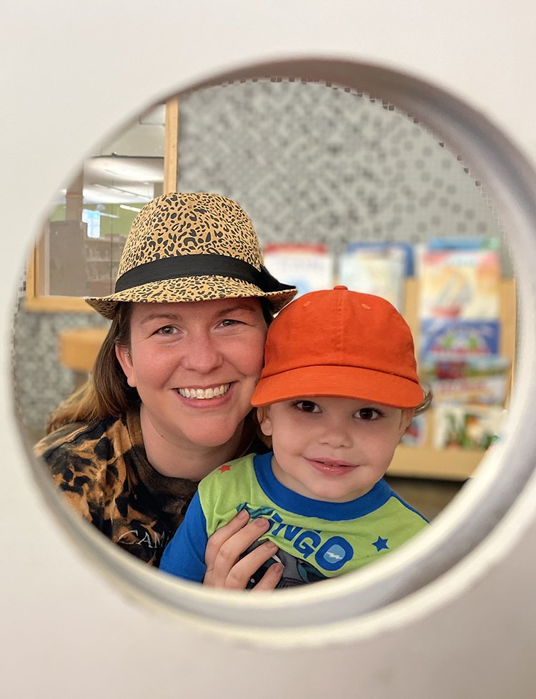 Mother and young toddler son wearing hats and smiling as they look through a circle at the camera